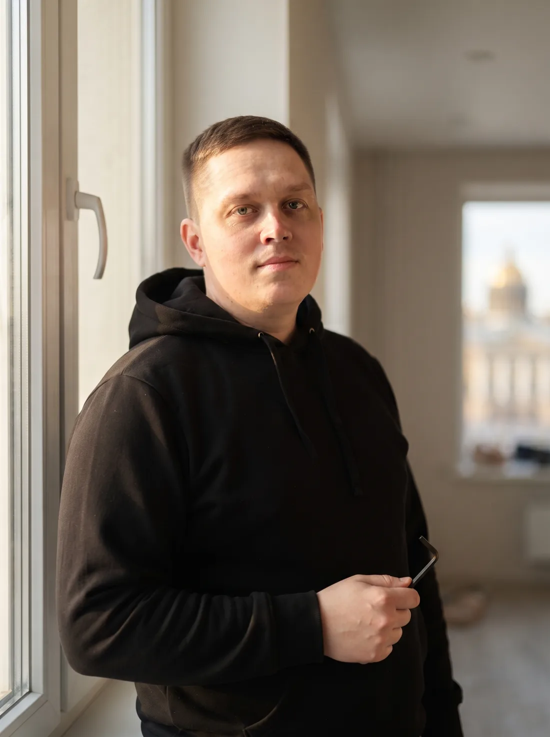 Александр — мастер по ремонту окон, у белого пластикового окна с шестигранником в руке